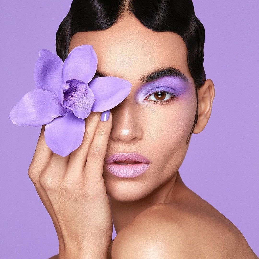 Close-up of a woman applying a beauty gadget to her face for skincare, with pastel lilac backdrop